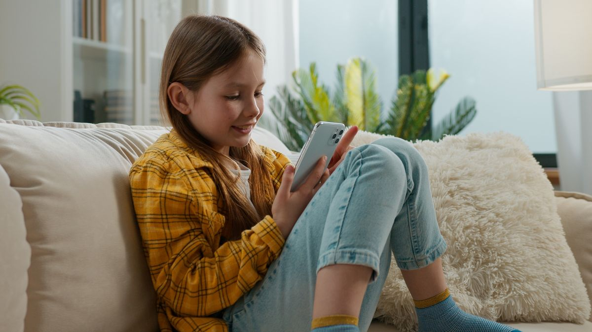 Dítě sedí na gauči přilepené k telefonu